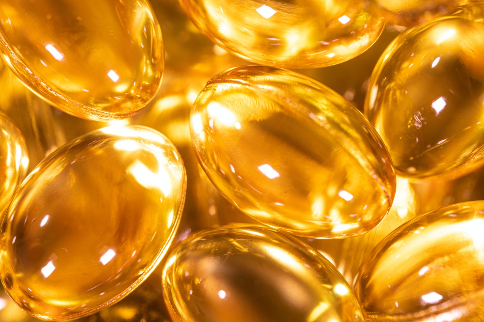 Detailní obrázek lesklé, průsvitné zlaté kapsle rybí olej, případně vitamíny nebo doplňky, seskupené dohromady. Kapsle odrážejí světlo a vytvářejí světelný efekt.