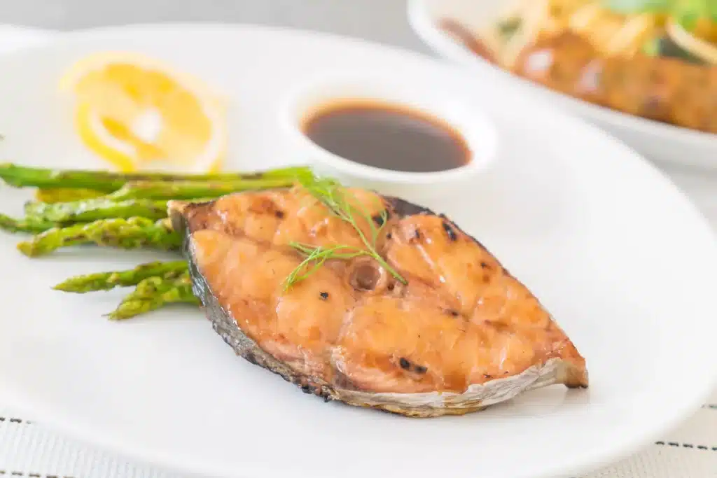 Šťavnatý lososový steak s kůží podávaný s chřestem, citronem a máslovou šťávou jako součást losos receptů