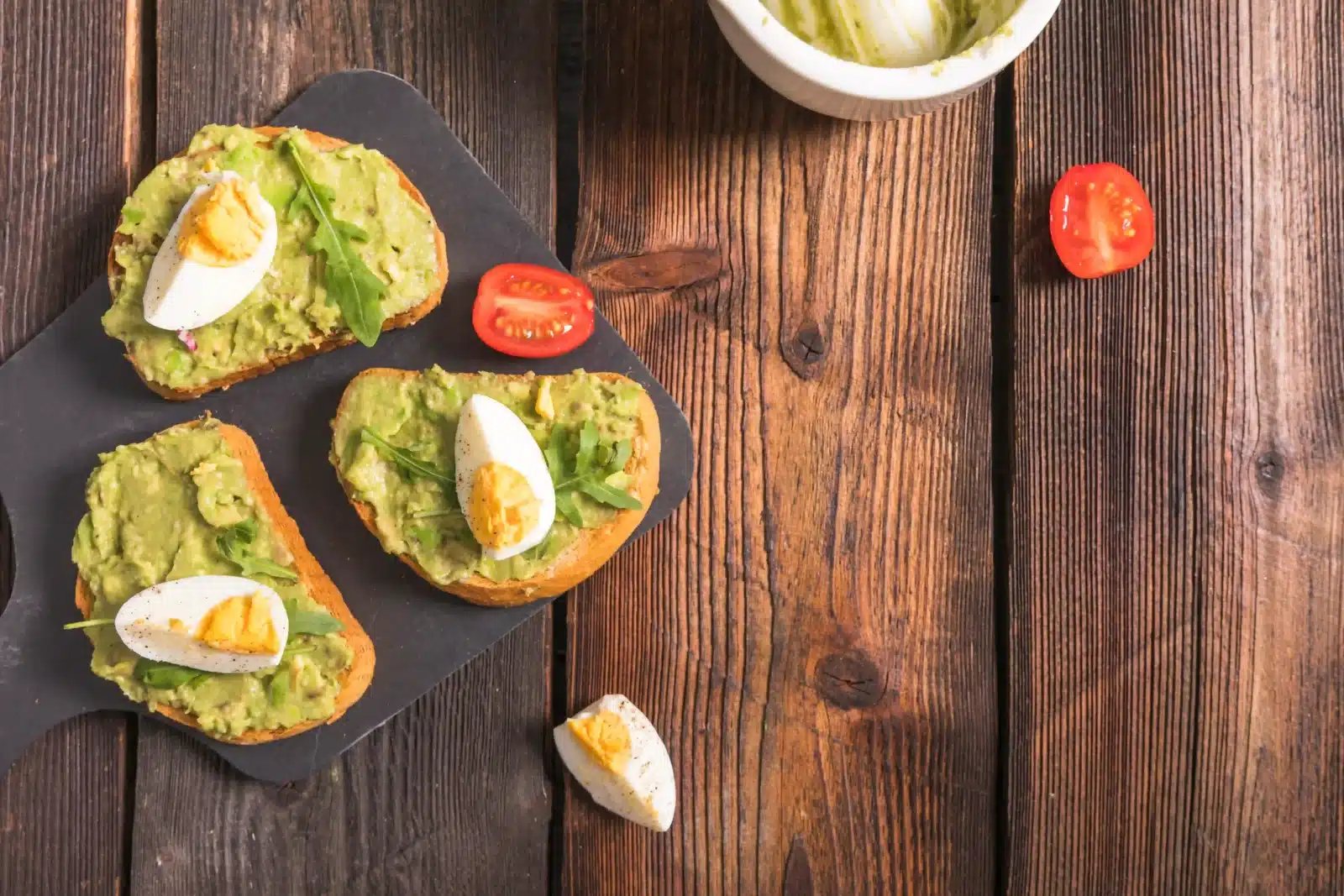 Recept z avokáda – toast s avokádovou pomazánkou, rukolou a vařeným vejcem, servírovaný s rajčaty.