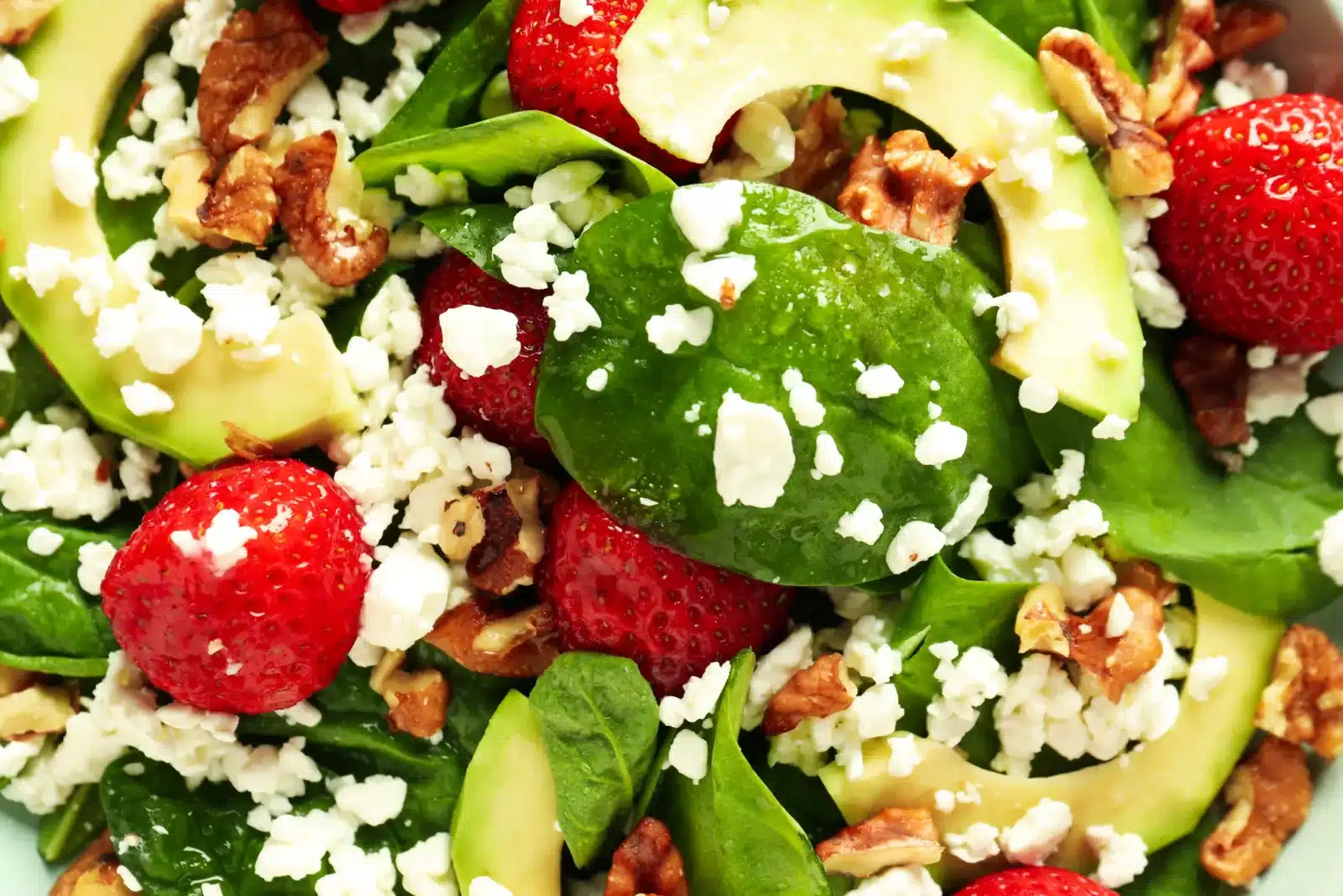 Gurmánský salát s čerstvým baby špenátem, plátky avokáda, jahodami, rozdroleným sýrem a vlašskými ořechy.